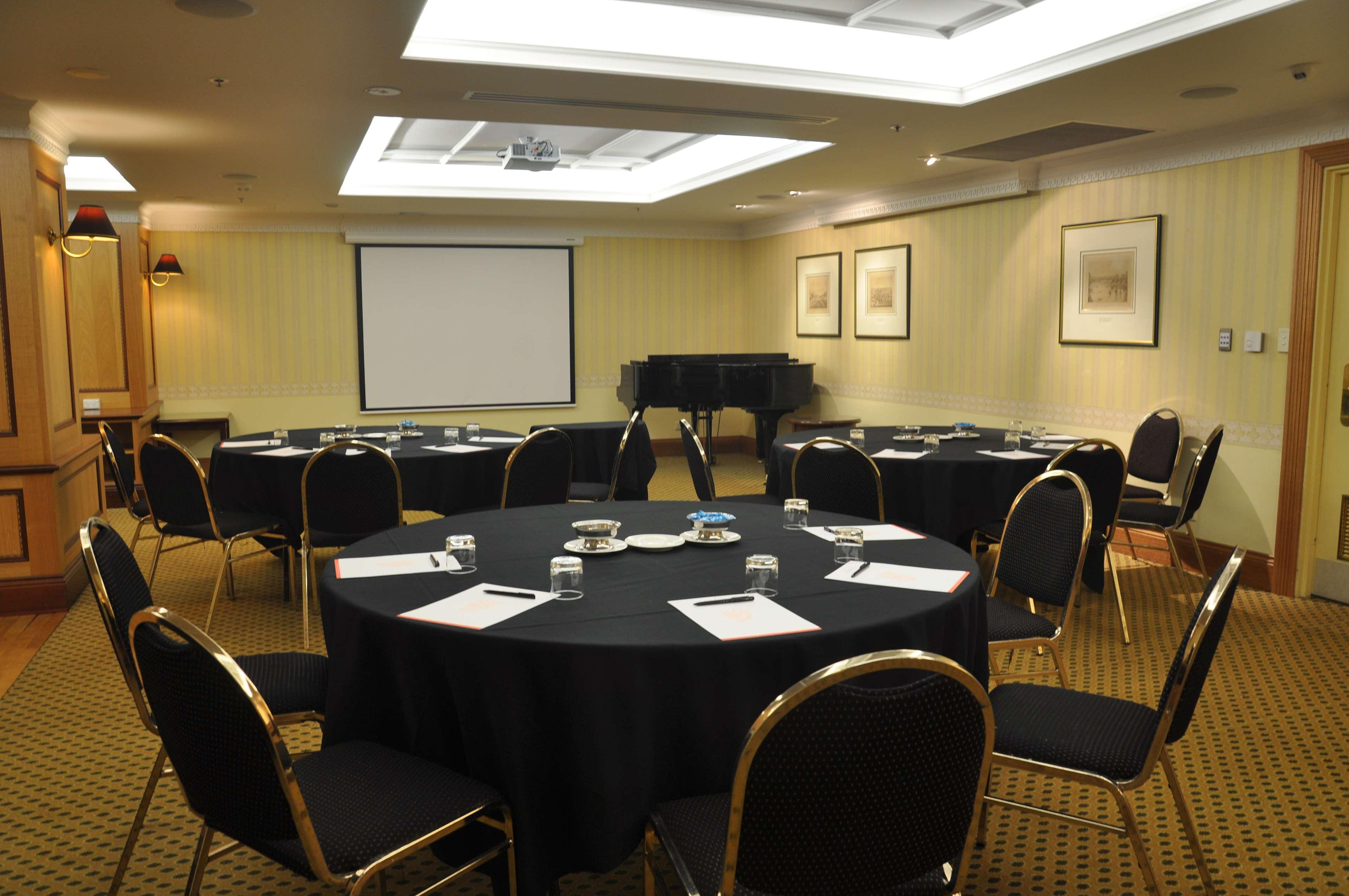 Hotel Stamford Plaza Adelaide Exteriér fotografie The photo shows a conference room set up for a meeting or presentation. There are several round tables covered with black tablecloths, each surrounded by black upholstered chairs. On the tables, there are notepads and glasses of water, indicating tha