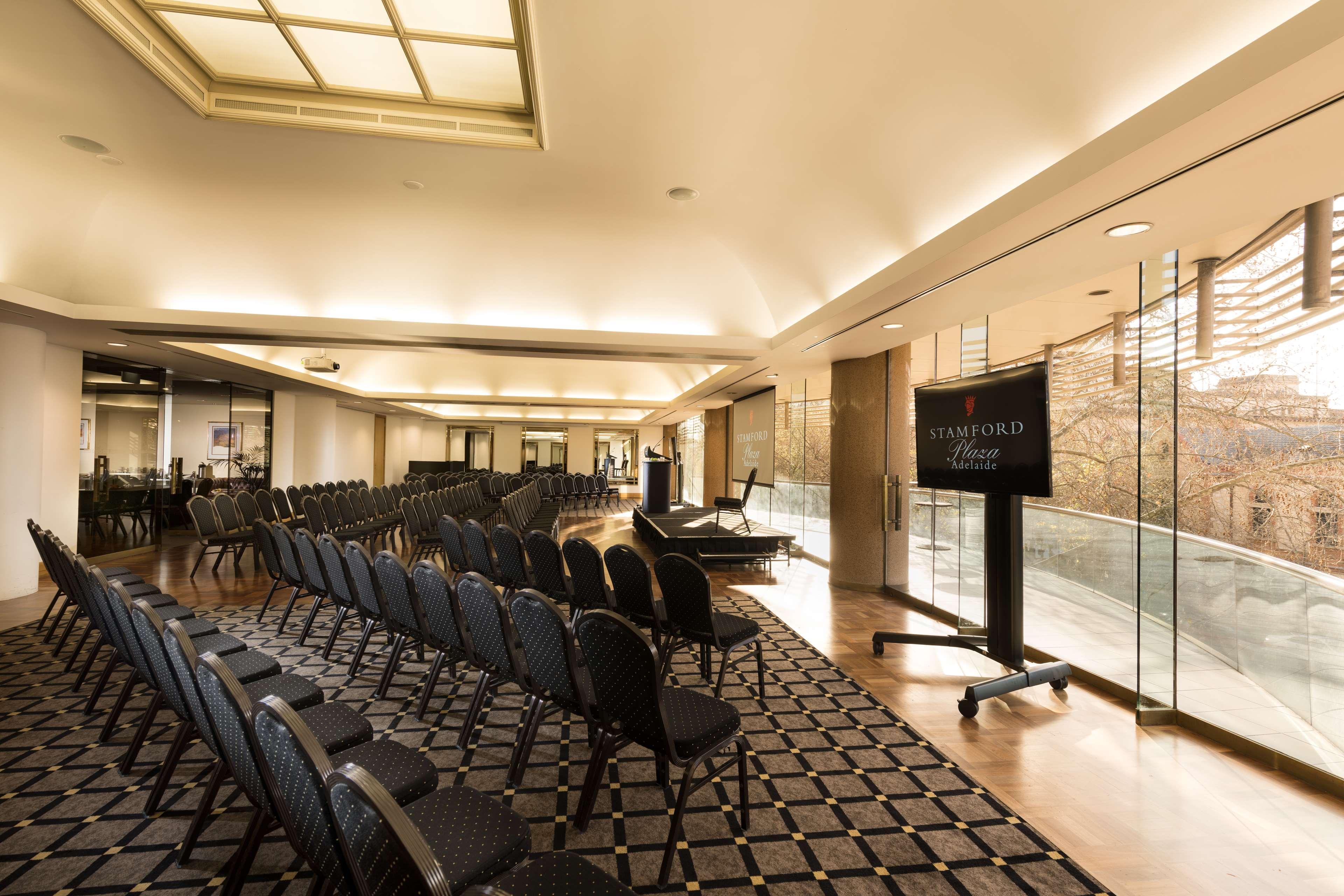 Hotel Stamford Plaza Adelaide Exteriér fotografie The photo shows a large, elegantly designed event space or meeting room. There are rows of black chairs set up facing a presentation area. The flooring features a patterned carpet, and large windows allow natural light to enter the room. On one side,