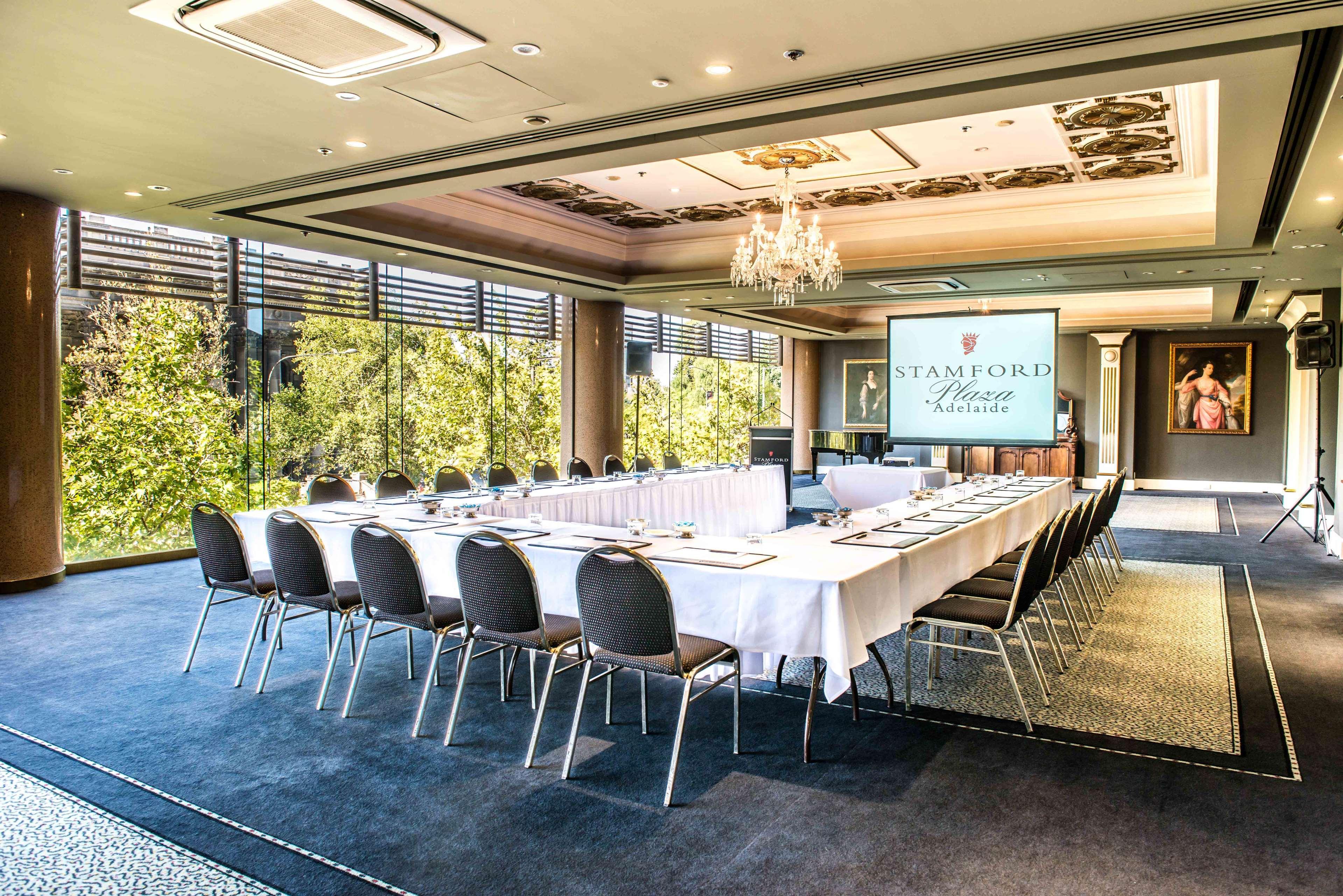 Hotel Stamford Plaza Adelaide Exteriér fotografie The photo shows a stylish conference room set up for a meeting or event. There is a long rectangular table covered with a white tablecloth, surrounded by black chairs. A large screen displays the name "Stamford" along with a logo. The room features l