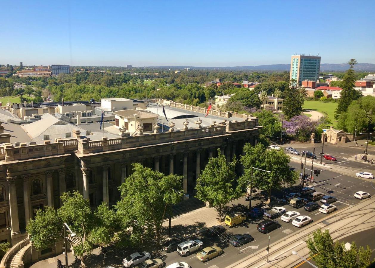 Hotel Stamford Plaza Adelaide Exteriér fotografie The photo depicts a cityscape view, showcasing a mix of architectural structures and greenery. In the foreground, there is a large, classical building with columns, suggesting it may be a historical or governmental structure. Surrounding the building